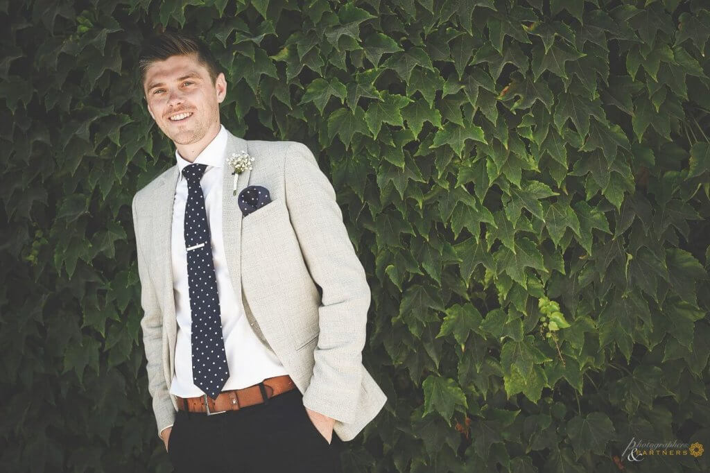 The groom stands in front of ivy leaves