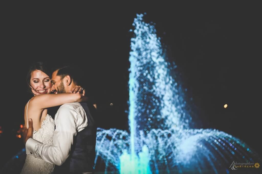 the couple embrace in front of fountain